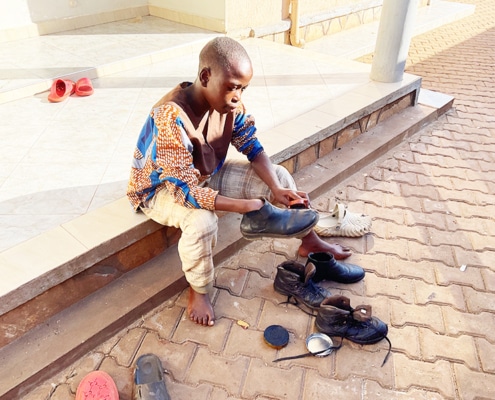 Former street child from Kampala cleaning his shoes